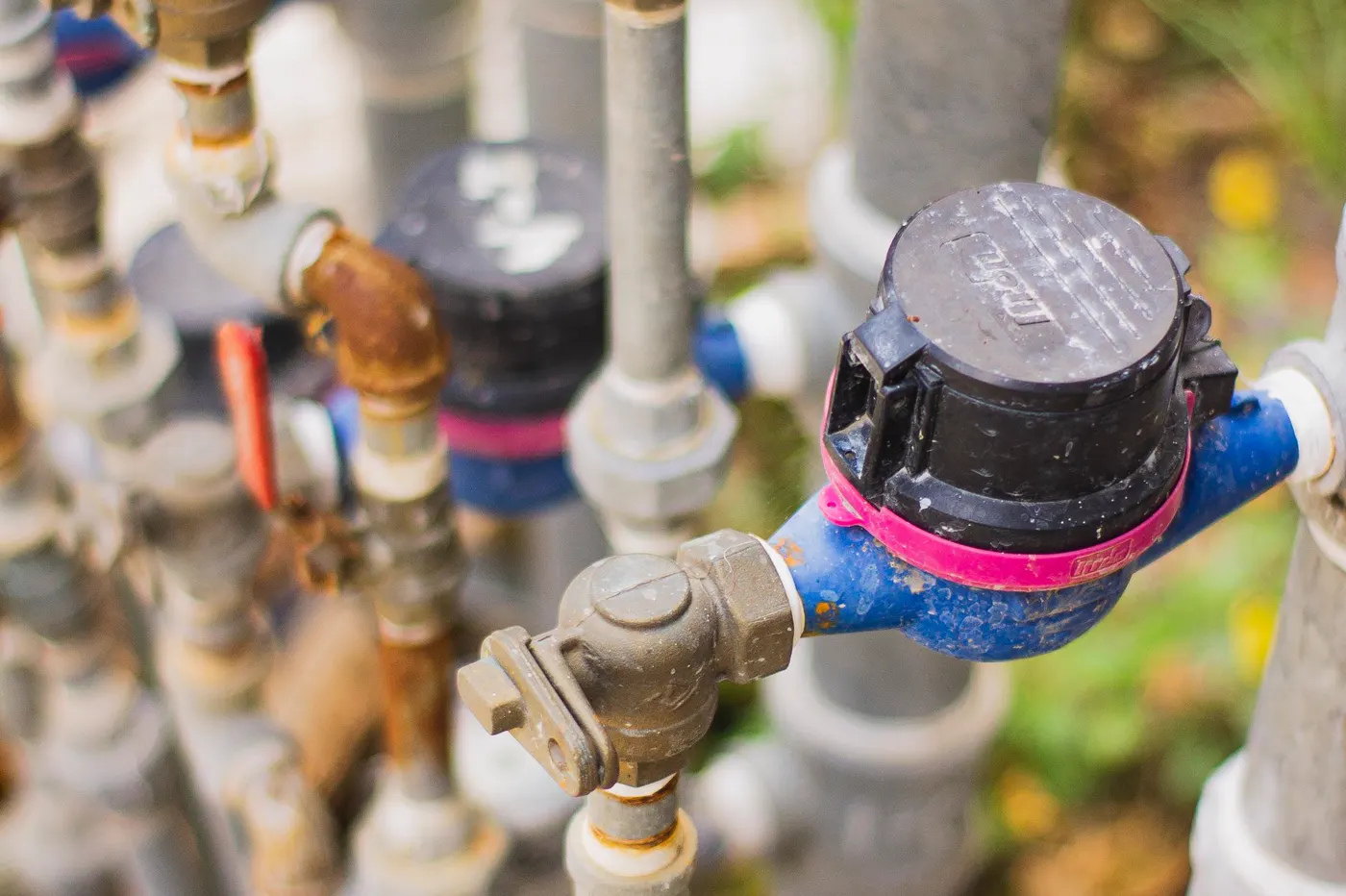 Close-up of a water meter connected to valves and outdoor pipes.