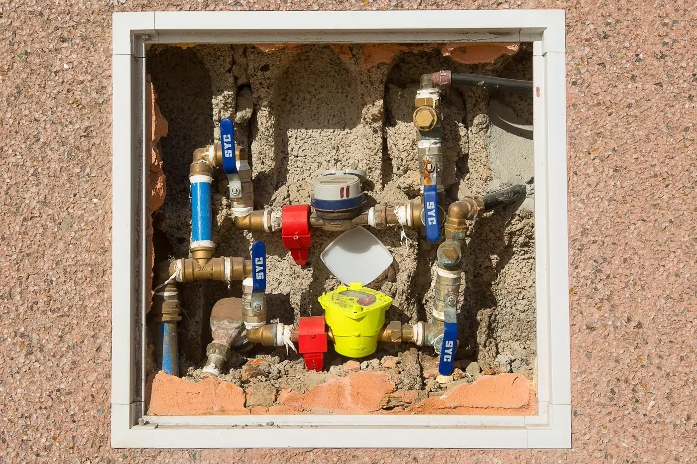 Two residential water meters and shutoff valves mounted inside a wall box.