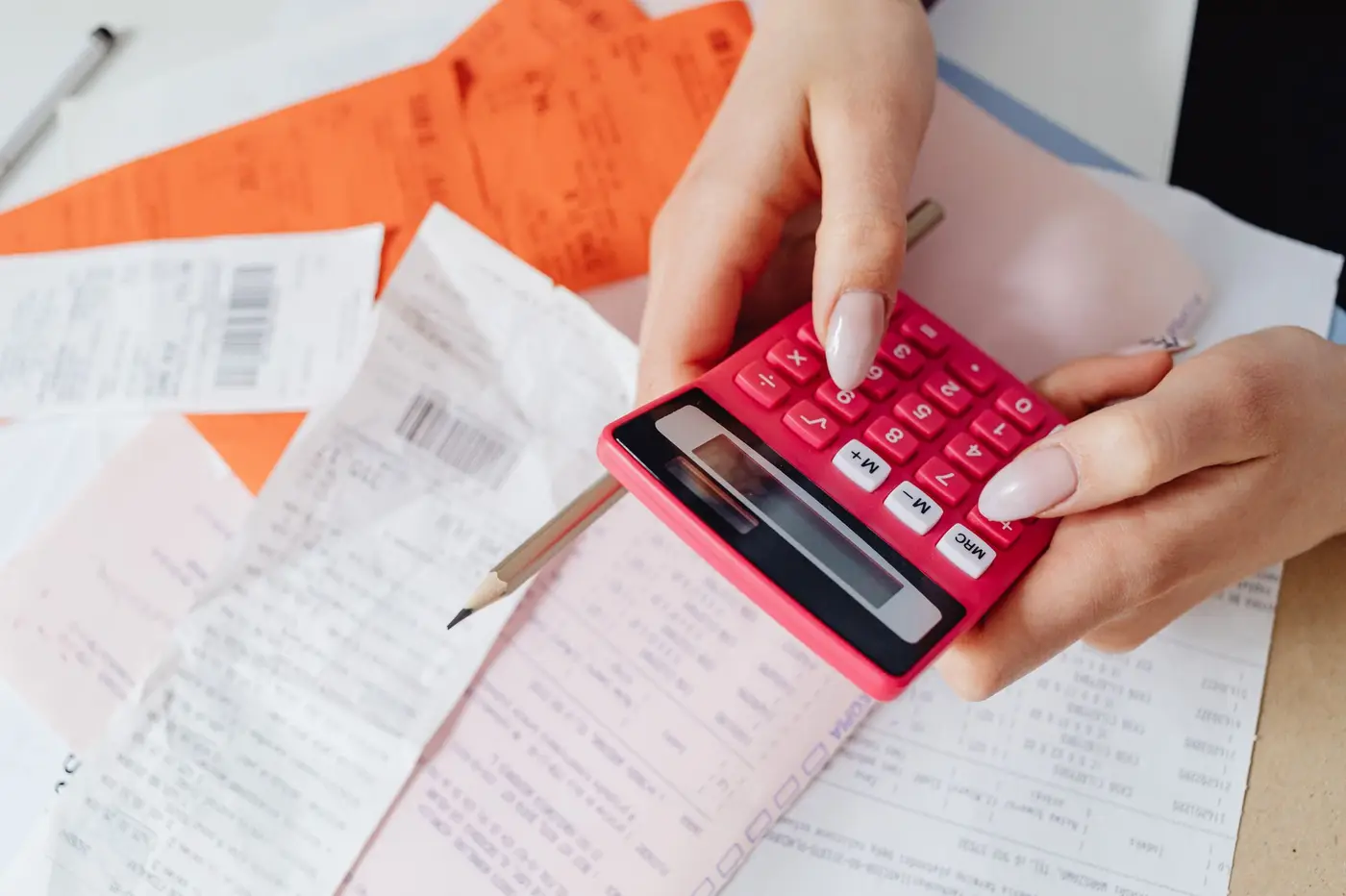 Hands using a pink calculator over a pile of receipts.