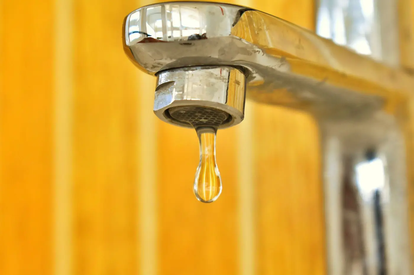 A drop of water hanging from a chrome faucet.
