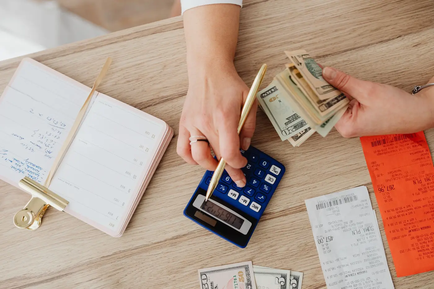 Hands counting cash beside a calculator, a notebook, and receipts.