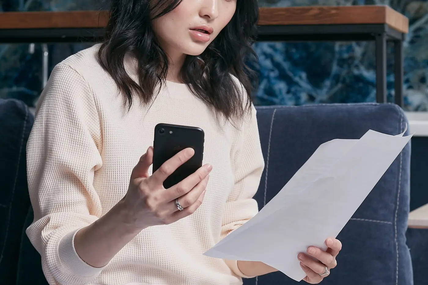 A woman on her phone while reading a paper bill.