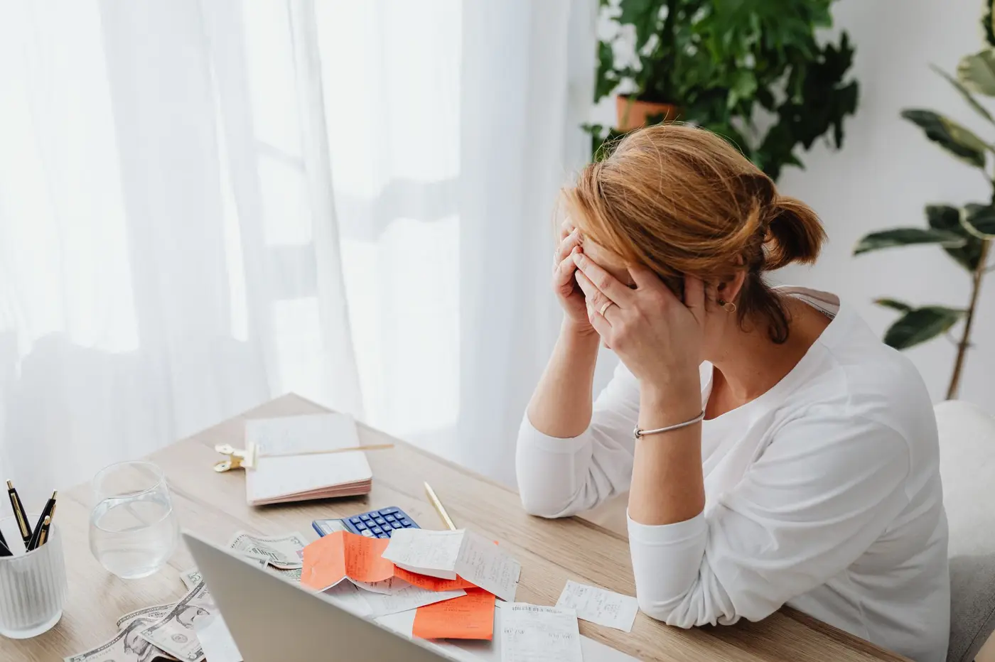 A stressed woman at a desk with bills, receipts, and a calculator.